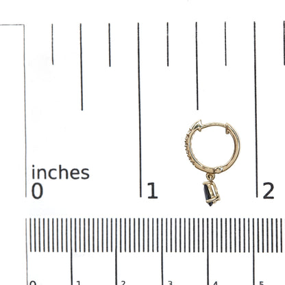 Close-up front angle of a yellow metal hoop earring with small white gemstones along the outer edge and a dangling pear-shaped blue gemstone, shown on a ruler for size reference.