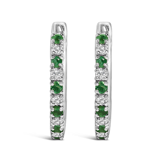 Front view of a pair of white metal hoop earrings set with alternating round white gemstones and green gemstones in prong settings.
