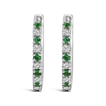 Front view of a pair of white metal hoop earrings set with alternating round white gemstones and green gemstones in prong settings.