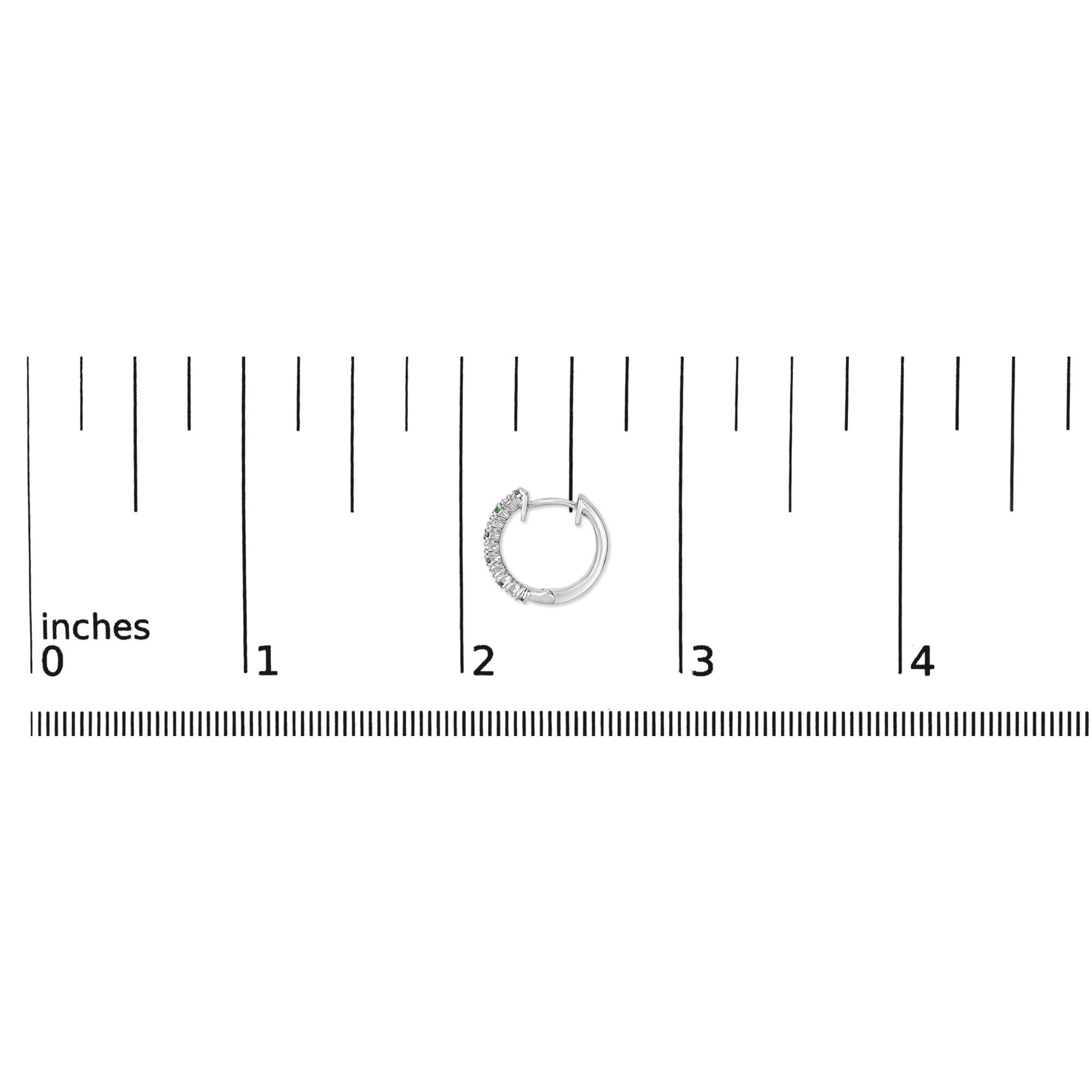 Close-up front angle of a white metal hoop earring with alternating round white and green gemstones set in prongs, shown on a ruler scale.