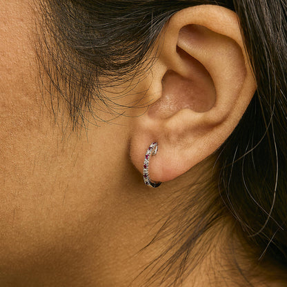 Close-up side view of a model wearing a white metal hoop earring adorned with round white gemstones and red gemstones in prong settings.