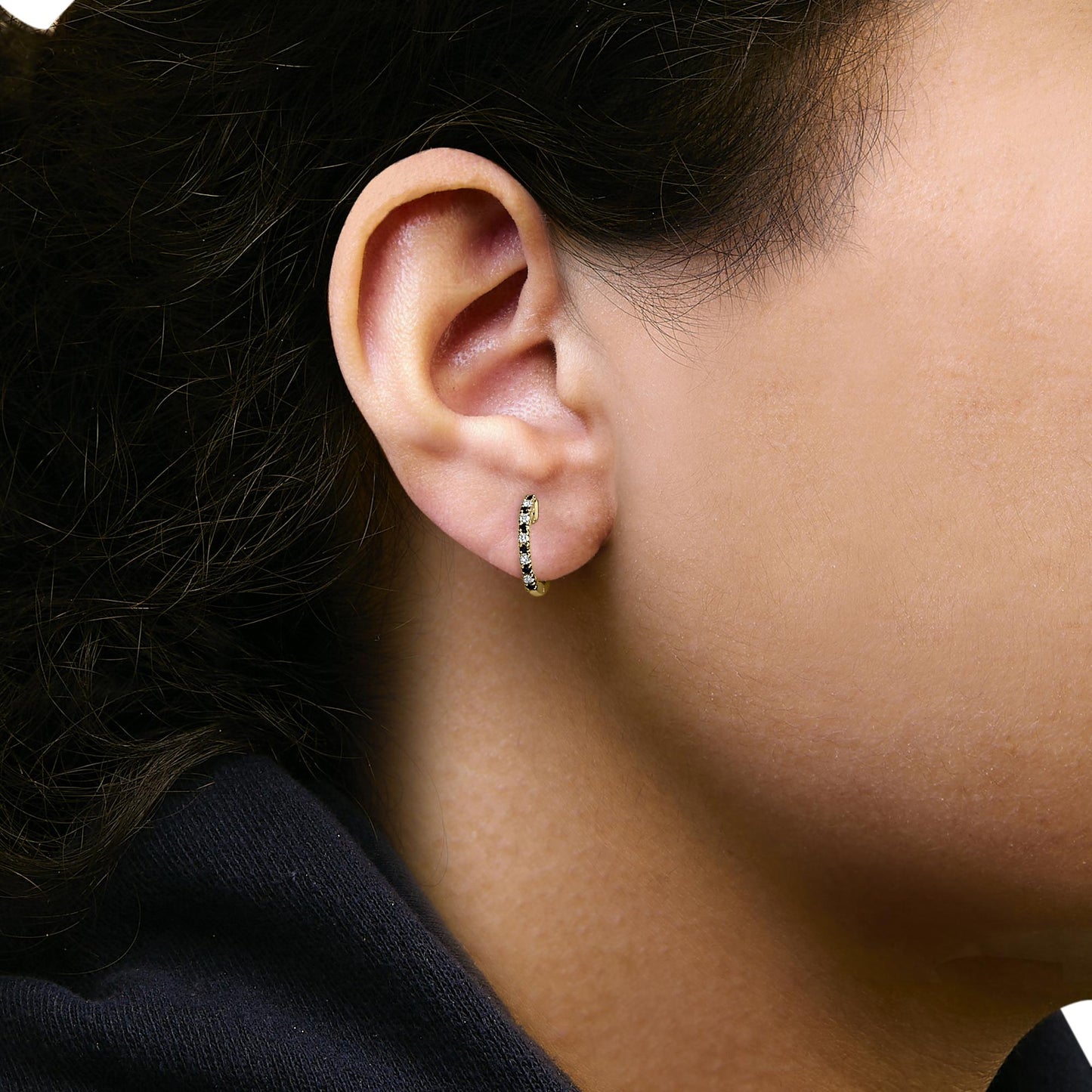 Close-up side view of a model wearing a small yellow metal hoop earring set with alternating white and blue round gemstones in a prong setting.