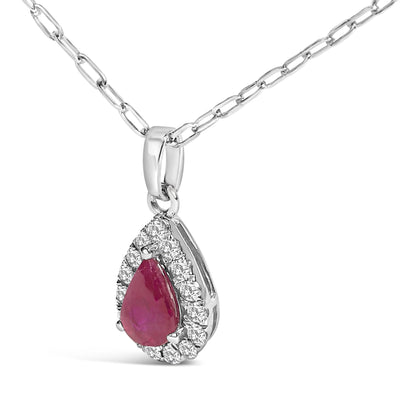 Close-up front angle of a white metal necklace with a pear-shaped red gemstone pendant surrounded by a halo of small round white gemstones in a micro-pave setting.