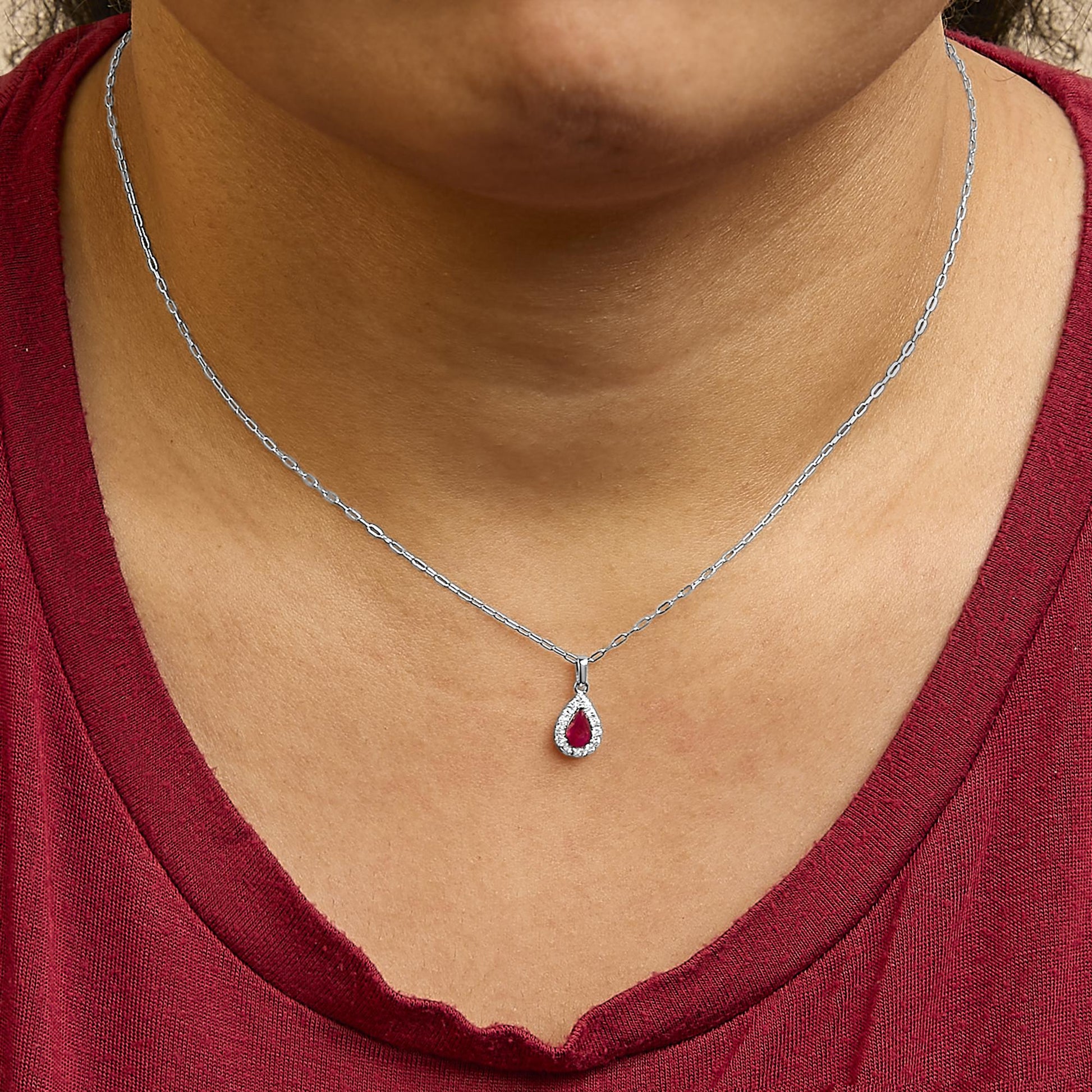 Necklace with a pear-shaped red gemstone pendant surrounded by small round white gemstones in micro-pave setting, shown worn on a model from a front angle.