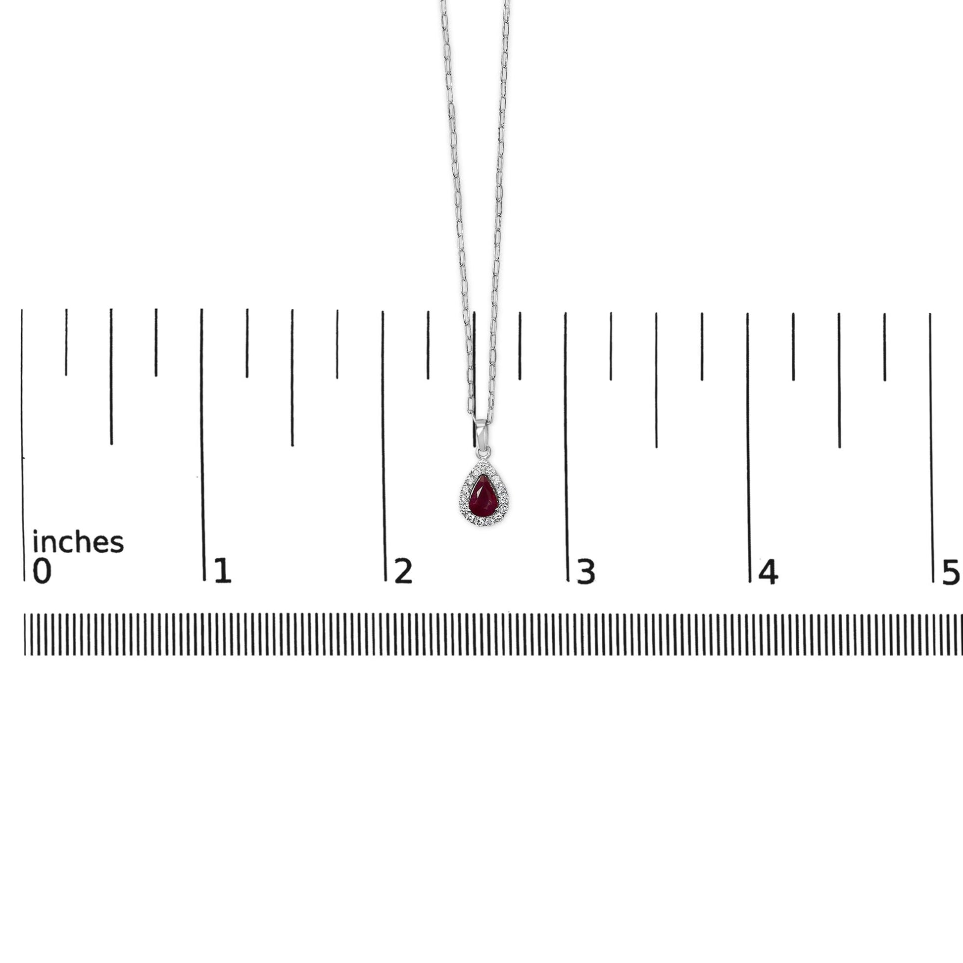 White necklace with a pear-shaped red gemstone pendant surrounded by small round white gemstones, shown on a scale with a top-down view.