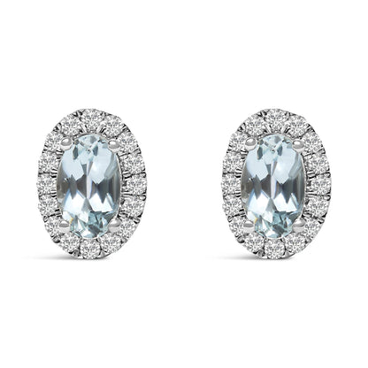 Front view of a pair of white metal oval earrings with a central blue oval gemstone surrounded by round white gemstones in a pave setting.