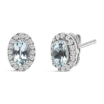 Front and side angled view of white metal stud earrings featuring oval blue gemstones surrounded by small round white gemstones in a pave setting.