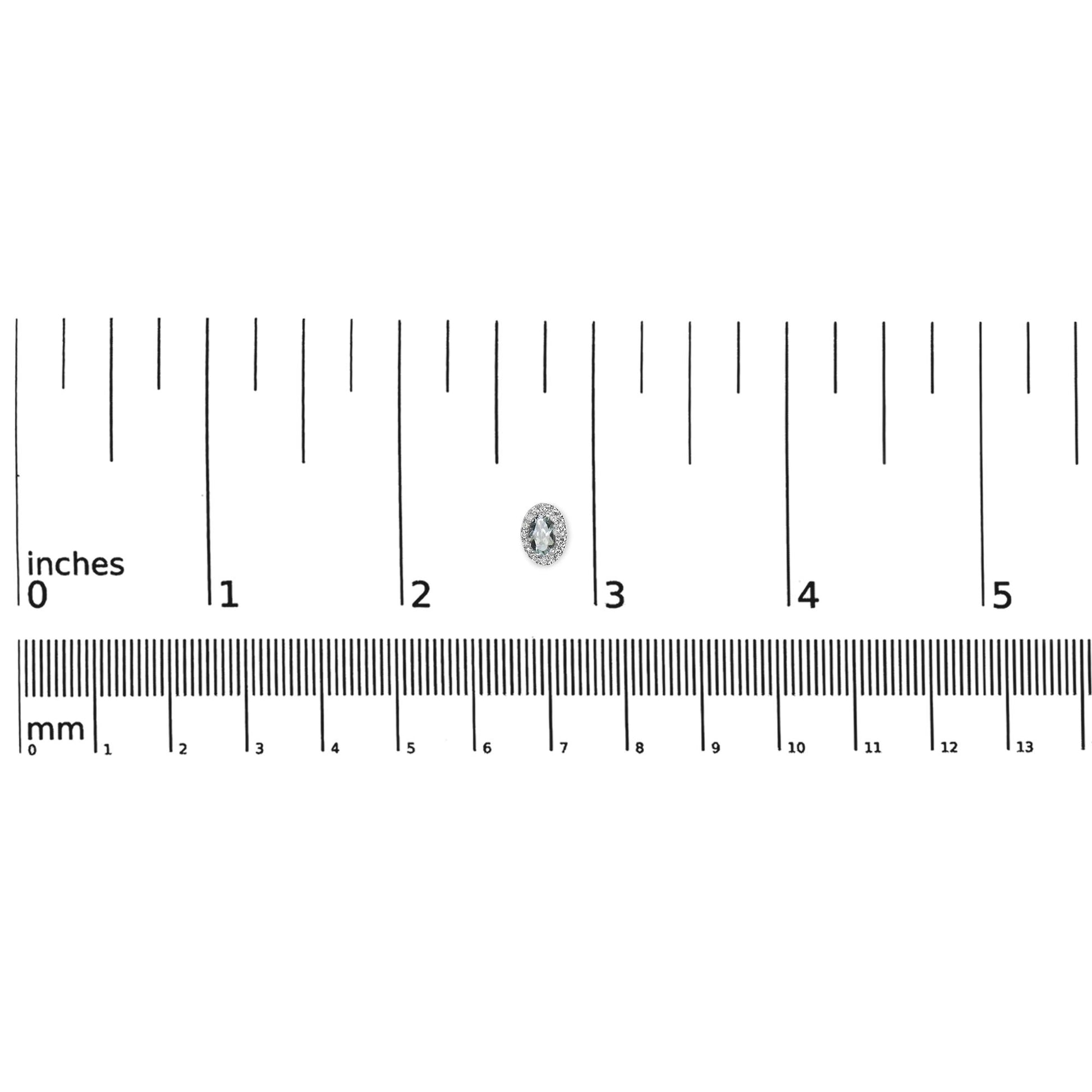 Close-up, top-down view of a single white earring with a blue oval gemstone surrounded by small white gemstones in a pave setting, placed on a ruler for size reference.