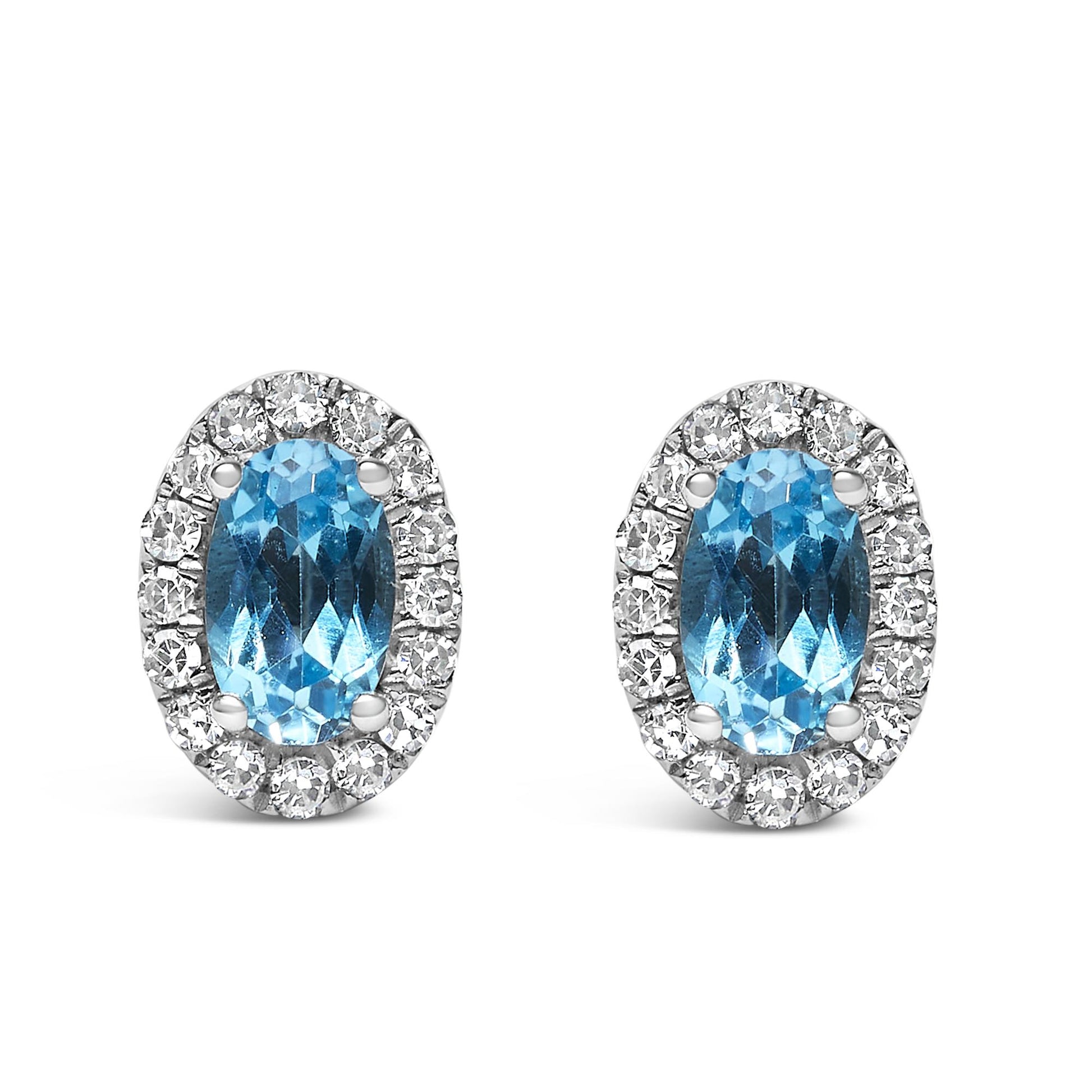 Front view of white metal oval earrings with central blue oval gemstones surrounded by a halo of small round white gemstones in pave setting.