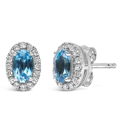 Close-up front and side angle view of white metal stud earrings with oval blue gemstones in 4-prong setting surrounded by a halo of round white gemstones in pave setting.