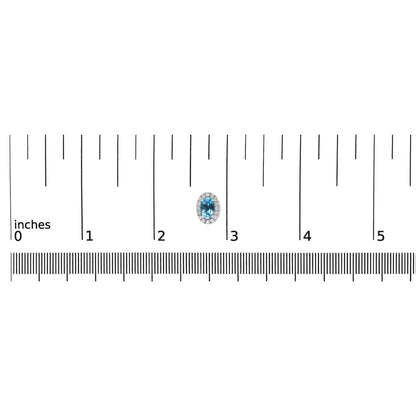 Close-up top-down view of a white metal oval-shaped earring with a blue oval gemstone surrounded by small white round gemstones in pave setting placed on a ruler for size reference.