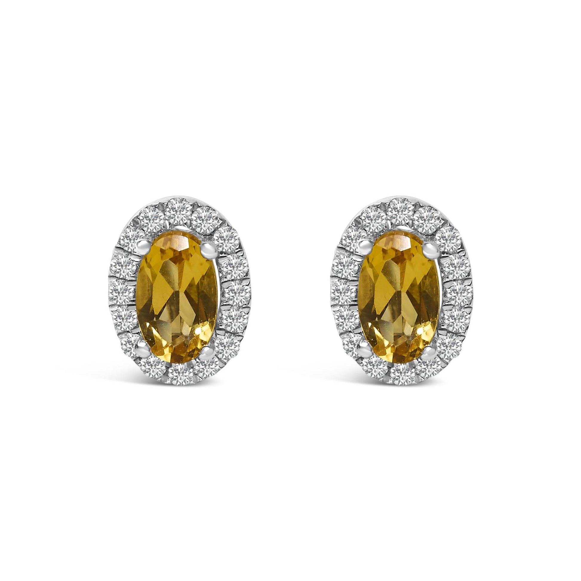 Pair of white metal stud earrings with oval yellow gemstones in four-prong settings, surrounded by a halo of small round white gemstones, shown from a front angle.