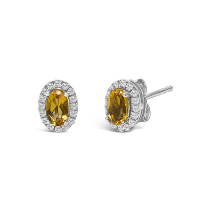 Pair of white metal stud earrings with oval yellow gemstones surrounded by small round white gemstones, shown at a slight angle.