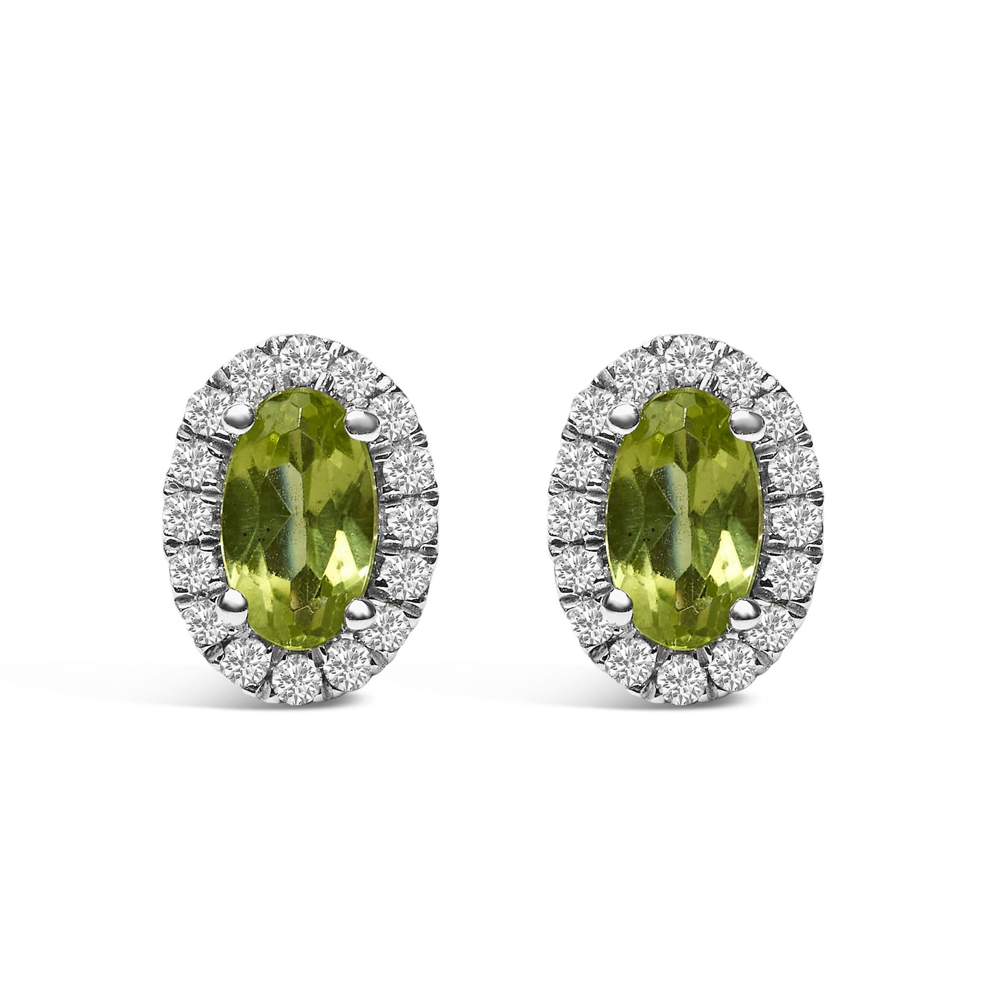 Front-facing shot of a pair of white metal oval earrings with green oval gemstones surrounded by a halo of small round white gemstones in pave setting.