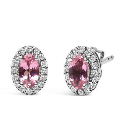 Pair of white metal stud earrings with oval pink gemstones surrounded by white round gemstones in pave setting, shown from a front and angled side view.