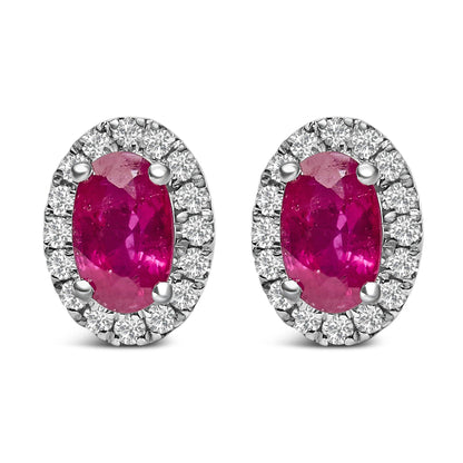 Pair of white metal oval earrings with central red oval gemstones surrounded by a halo of small round white gemstones, shown from front angle.