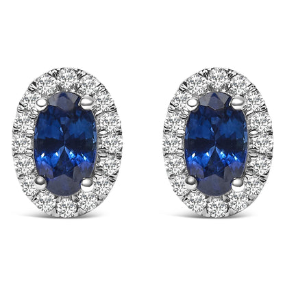 Front view of white metal oval earrings featuring blue oval gemstones surrounded by small round white gemstones in pave setting.