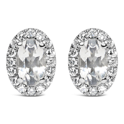Front angle view of white metal oval-shaped stud earrings with central oval white gemstones in four-prong settings, surrounded by a pave setting of round white gemstones.