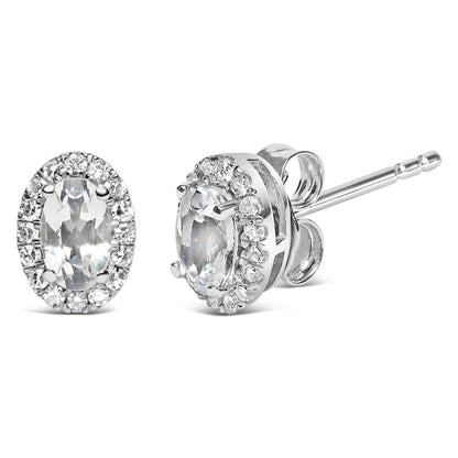Pair of white metal stud earrings with oval white gemstones surrounded by a halo of round white gemstones, shown in a front and side angled view.