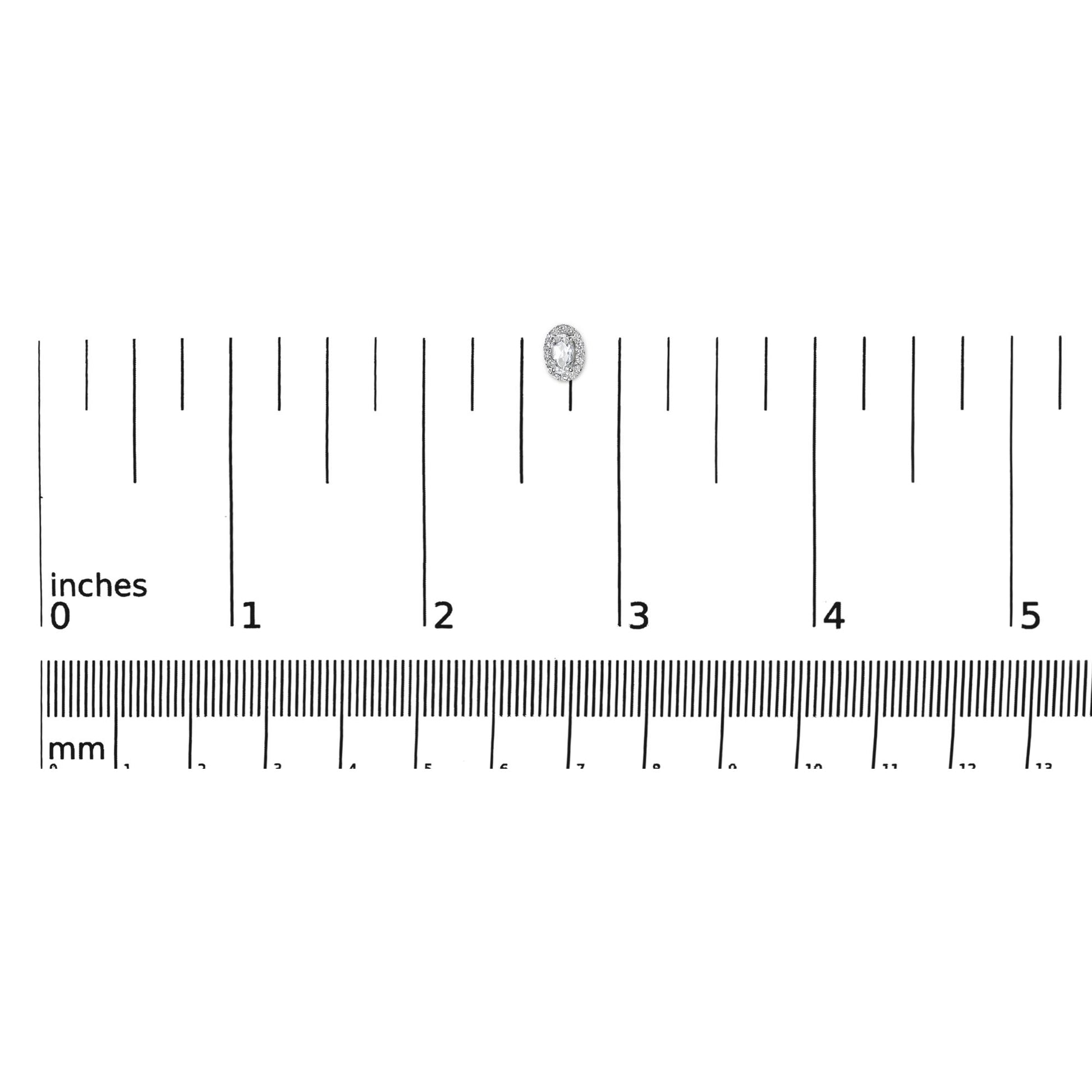 Top down view of a white metal earring with an oval white gemstone surrounded by small round white gemstones, placed on a ruler for size reference.