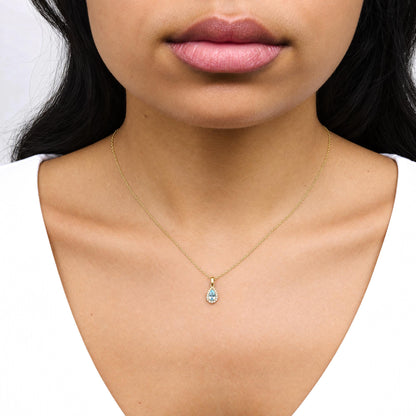 Close-up front view of a model wearing a yellow metal necklace with a pear-shaped blue gemstone pendant surrounded by round white gemstones in prong settings.
