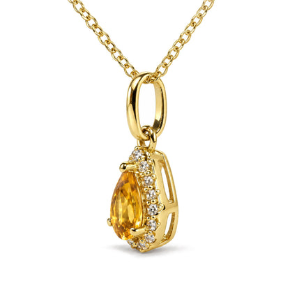 Close-up front angle of a yellow metal necklace with an oval link and a pear-shaped yellow gemstone pendant surrounded by small round white gemstones in prong settings.