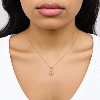 Close-up front view of a model wearing a yellow metal necklace featuring a pear-shaped yellow gemstone pendant surrounded by round white gemstones in a prong setting.