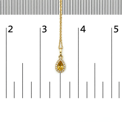 Yellow metal necklace with a pear-shaped yellow gemstone pendant surrounded by round white gemstones in a prong setting, shown on a scale from above.