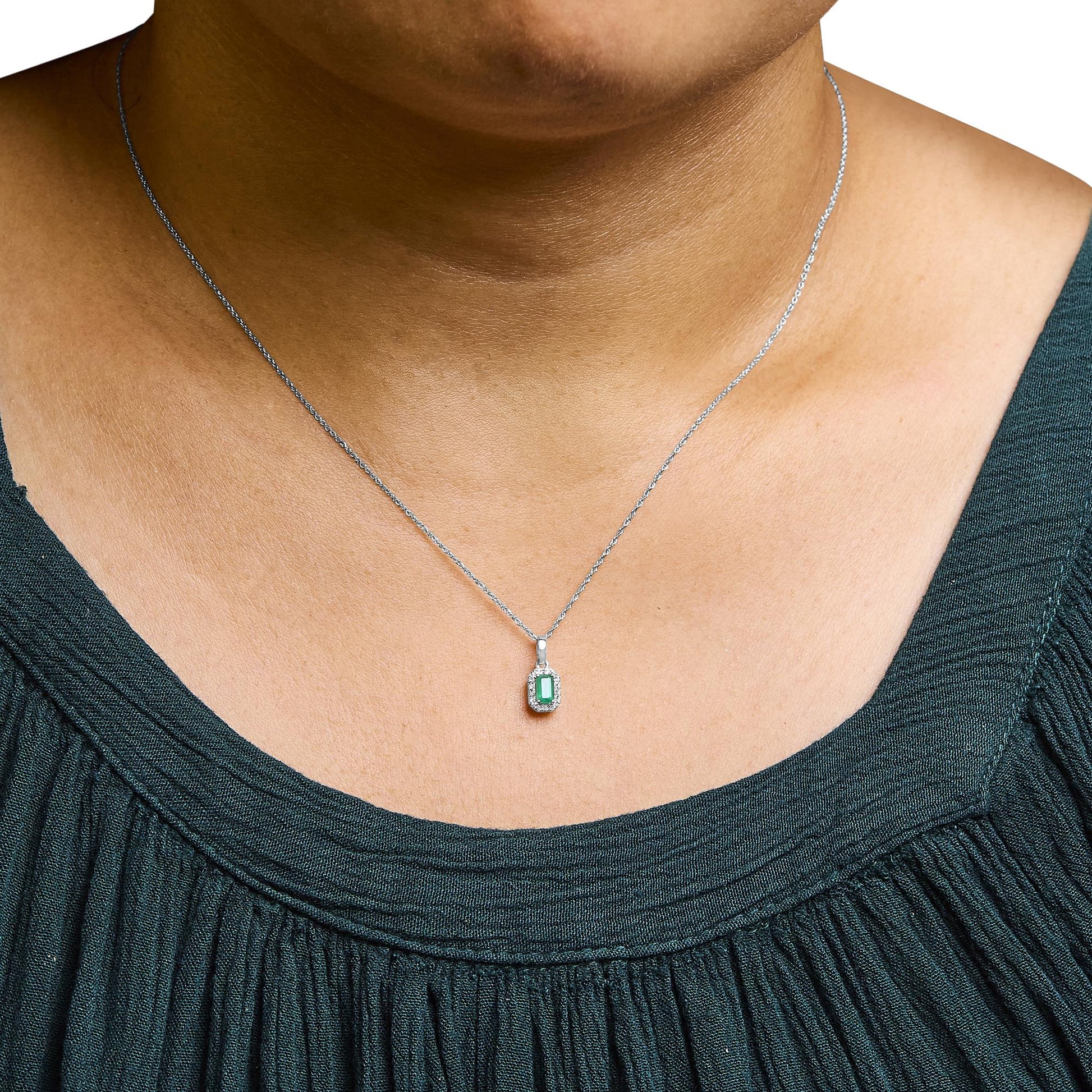 Close-up front view of a white metal necklace with a rectangular green gemstone pendant surrounded by small white gemstones, worn on a model.