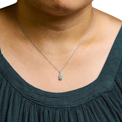 Close-up front view of a white metal necklace with a rectangular green gemstone pendant surrounded by small white gemstones, worn on a model.