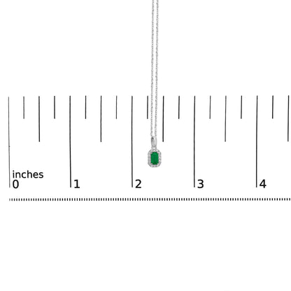 White metal necklace with a rectangular green gemstone pendant surrounded by small round white gemstones in micro-pave setting, shown from the front on a ruler for size reference.