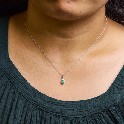 White metal necklace with oval green gemstone pendant surrounded by small round white gemstones in micro-pave setting, shown on a model from the front.