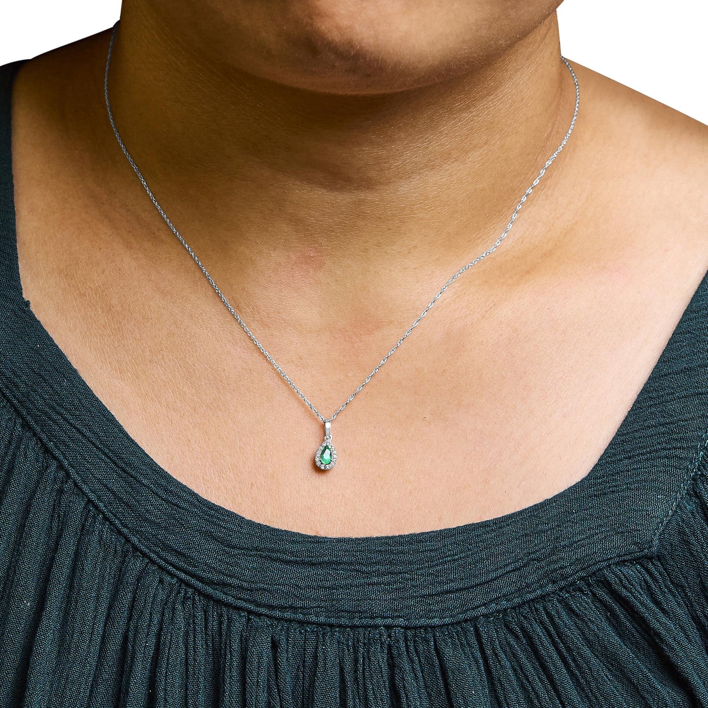 White metal necklace with a pear-shaped green gemstone pendant surrounded by small white gemstones, shown on a model from a front angle.