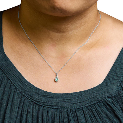 White metal necklace with a pear-shaped green gemstone pendant surrounded by small white gemstones, shown on a model from a front angle.