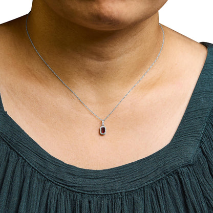 Close-up front view of a white metal necklace on a model, featuring a pendant with a red gemstone in an emerald shape, surrounded by small round white gemstones in micro-pave setting.