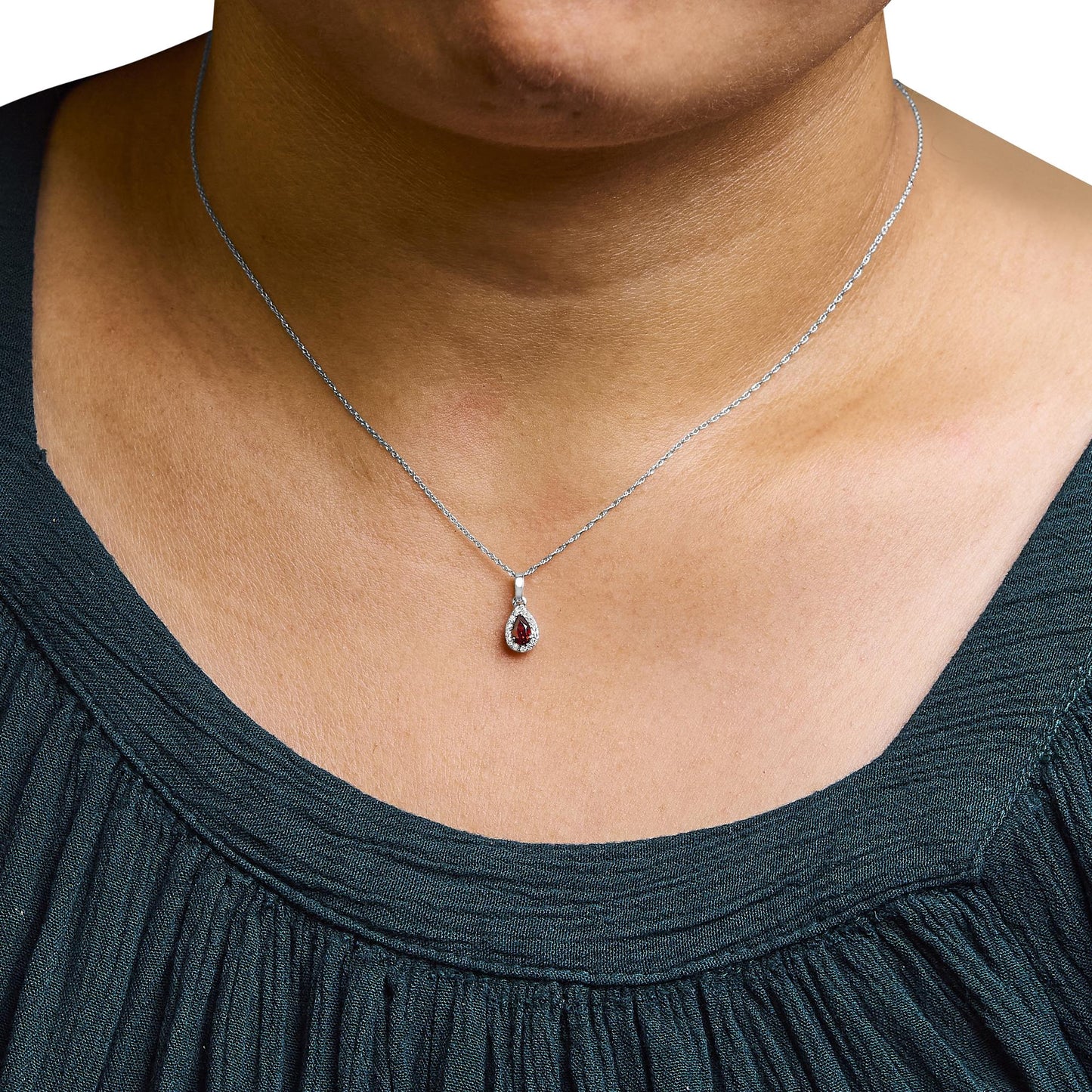 Close-up front view of a white necklace on a model featuring a pear-shaped red gemstone pendant surrounded by micro-pave set round white gemstones.