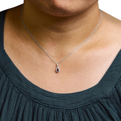 Close-up front view of a white necklace on a model featuring a pear-shaped red gemstone pendant surrounded by micro-pave set round white gemstones.