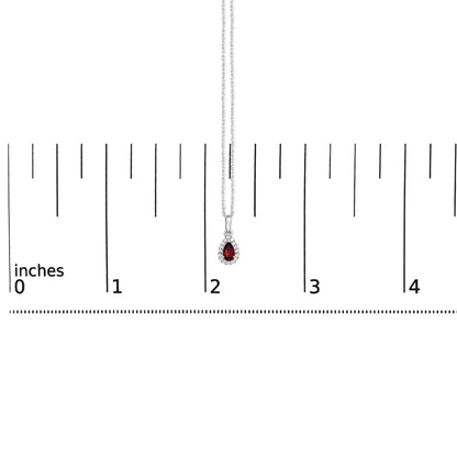 White metal necklace with a pear-shaped red gemstone pendant surrounded by round white gemstones, shown hanging vertically over a ruler for size reference.