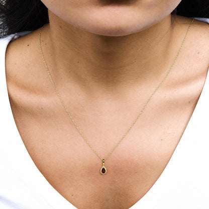 Close-up front view of a model wearing a yellow metal necklace with a pear-shaped red gemstone pendant surrounded by round white gemstones.