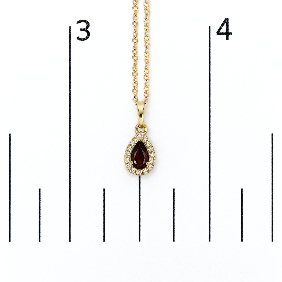 Close-up front view of a yellow metal necklace with a pear-shaped red gemstone pendant surrounded by white round gemstones, shown on a scale.