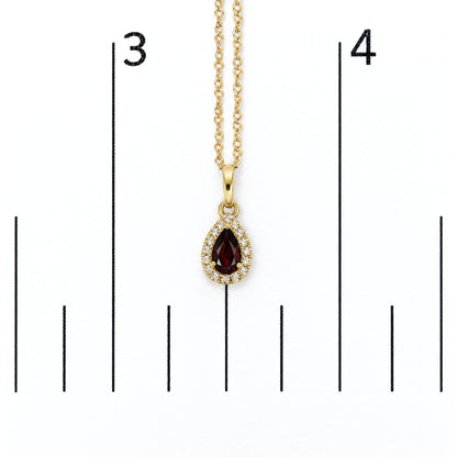 Close-up front view of a yellow metal necklace with a pear-shaped red gemstone pendant surrounded by white round gemstones, shown on a scale.