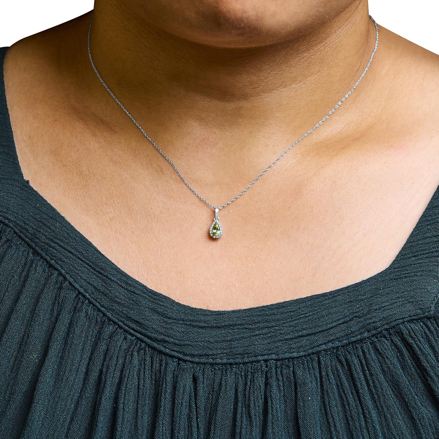 White metal necklace with a pear-shaped yellow gemstone pendant surrounded by small white gemstones in micro-pave setting, shown from the front on a model wearing a dark green top.