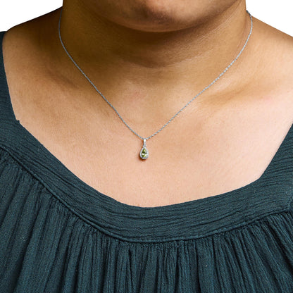 White metal necklace with a pear-shaped yellow gemstone pendant surrounded by small white gemstones in micro-pave setting, shown from the front on a model wearing a dark green top.