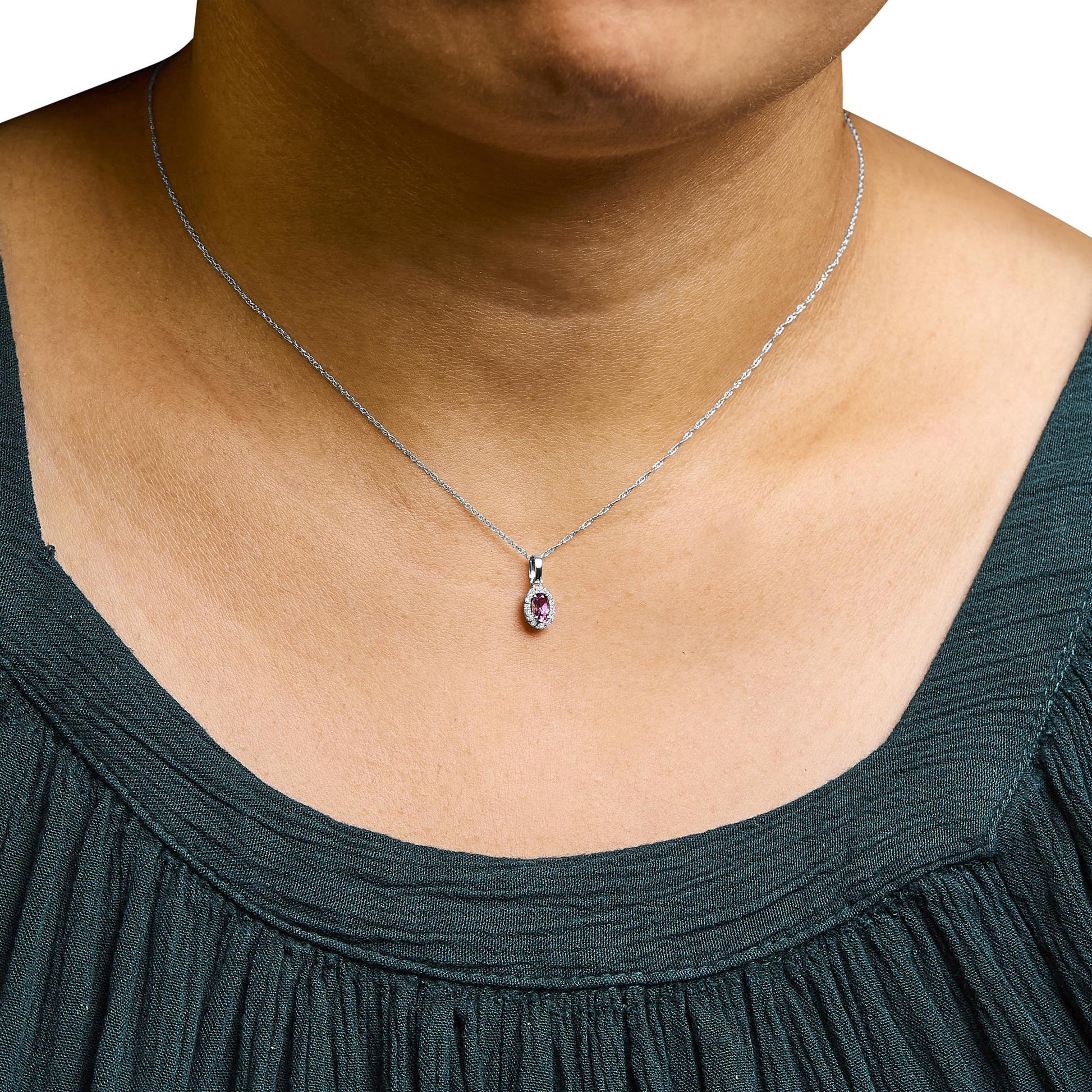Close-up front view of a white necklace on a model, featuring a pear-shaped pink gemstone pendant surrounded by small round white gemstones in a micro-pave setting.