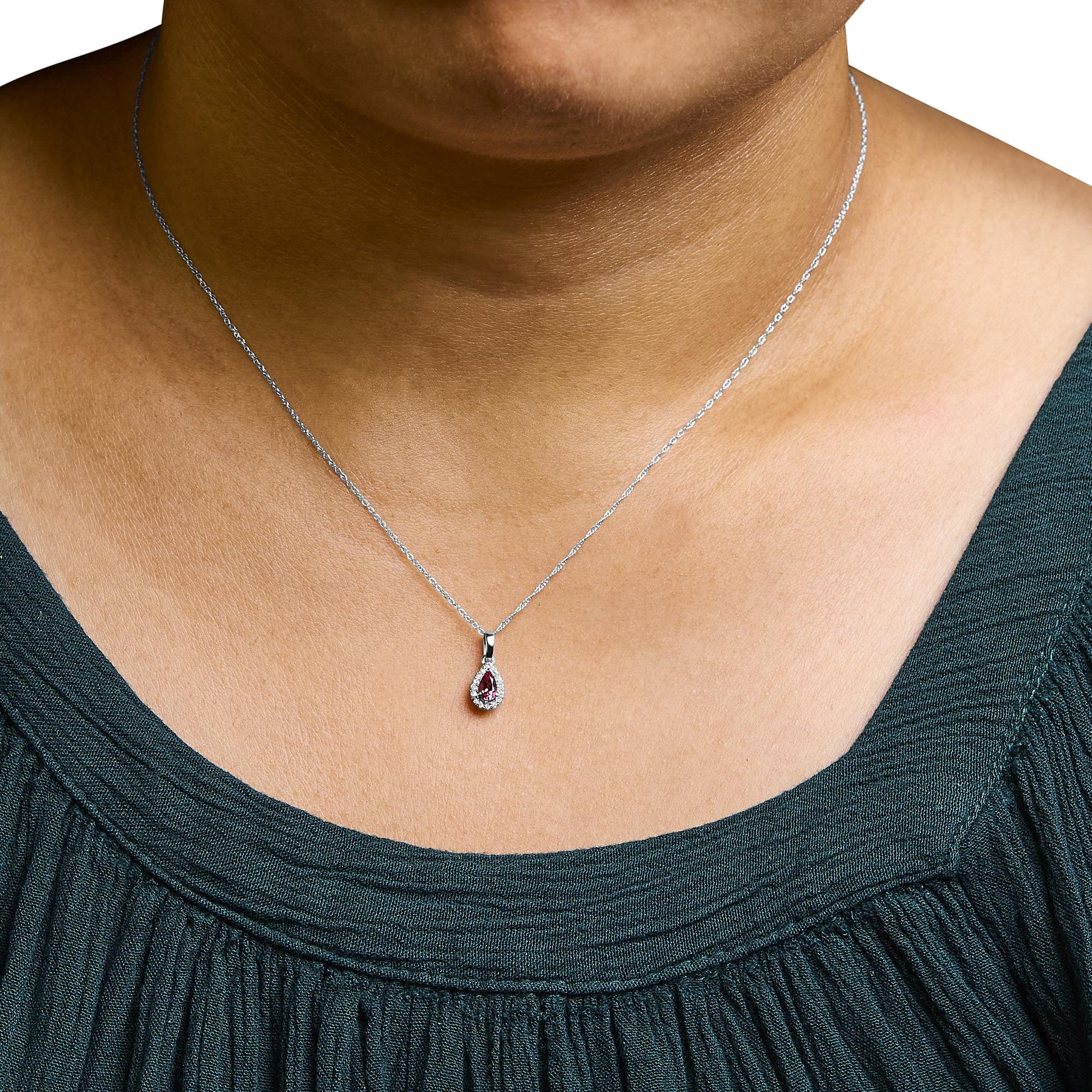 Close-up front view of a white metal necklace on a model, featuring a pendant with a pink emerald-shaped gemstone surrounded by small white round gemstones in micro-pave setting.