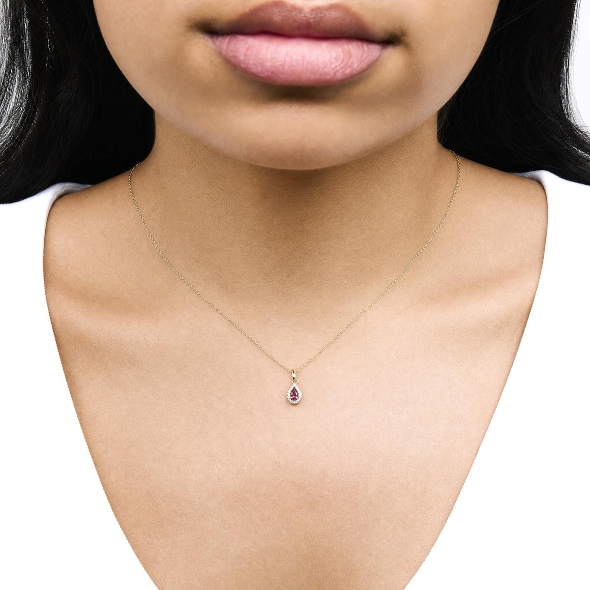 Close-up front view of a model wearing a delicate yellow metal necklace with a pear-shaped pink gemstone pendant surrounded by round white gemstones in prong settings.