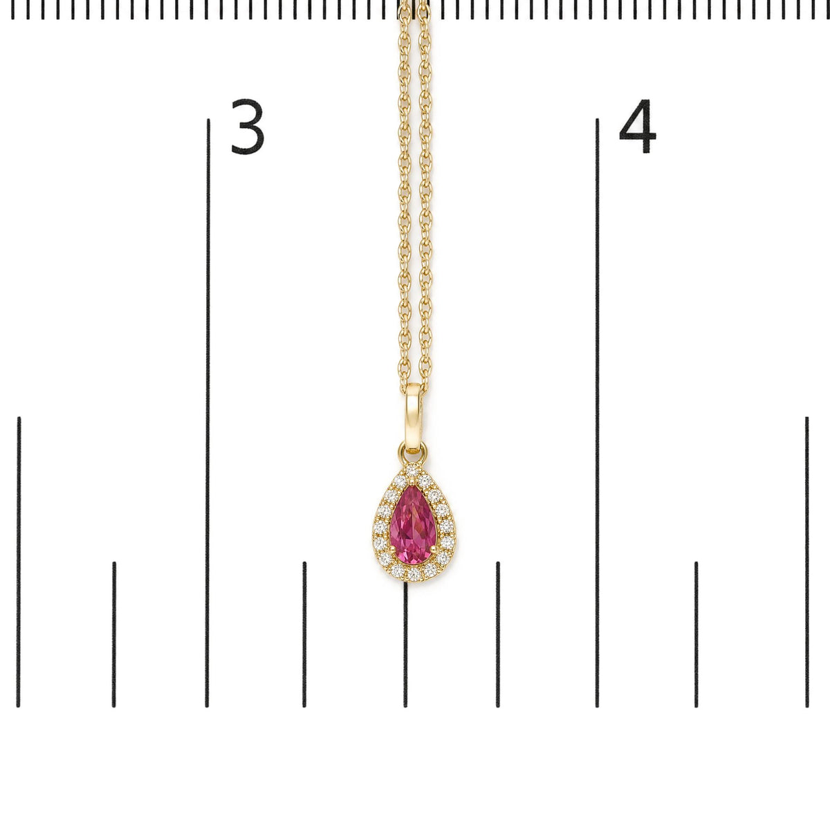 Close-up front view of a yellow metal necklace with a pear-shaped pink gemstone pendant surrounded by small round white gemstones, shown on a scale.