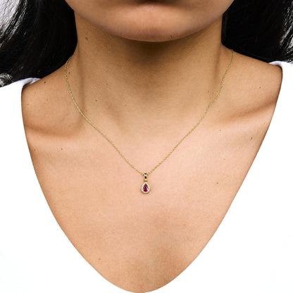 Close-up front view of a model wearing a yellow necklace with a pear-shaped red gemstone pendant surrounded by small round white gemstones in a prong setting.