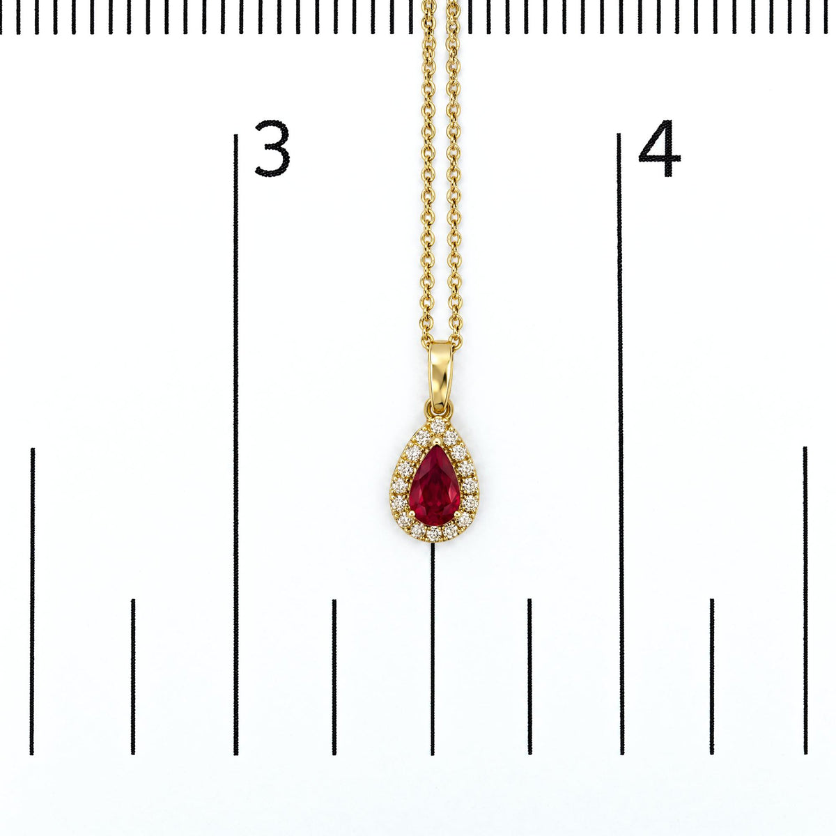 Close-up front view of a yellow metal necklace pendant with a pear-shaped red gemstone surrounded by round white gemstones, shown on a scale.