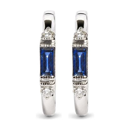 Close-up front view of a pair of white metal earrings featuring a round white gemstone in prong settings near the top and bottom, and a blue baguette-shaped gemstone in a channel setting in the center, shown on a white background.